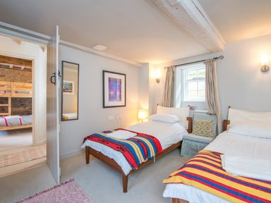 A bedroom with two single beds colorful blankets a chair and a window at Leeward Cottage in Cosheston near Pembroke Dock