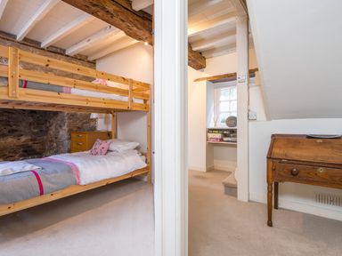 A bedroom with wooden bunk beds and stone wall and an adjacent area with a wooden desk and a window at Leeward Cottage in Cosheston near Pembroke Dock