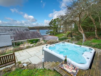 A hot tub on a patio with a bottle and glasses overlooking rooftops and a body of water at Leeward Cottage in Cosheston near Pembroke Dock