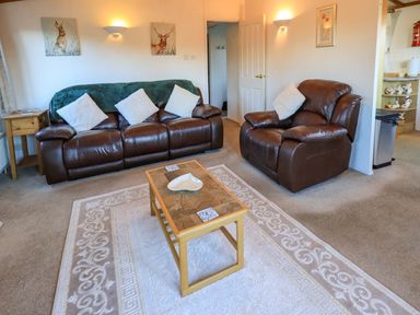 A living room with brown leather sofa and armchair a wooden coffee table and decorative wall art at Lavender Lodge in South Lakeland Leisure Village