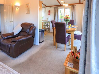 A living room with a brown leather armchair and dining area with table and four chairs at Lavender Lodge South Lakeland Leisure Village
