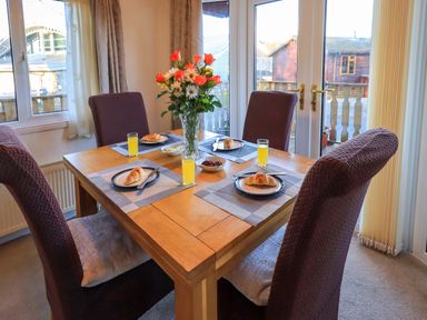 A dining table set with four plates each with a croissant and a glass of orange juice with a vase of flowers in the center at Lavender Lodge in South Lakeland Leisure Village