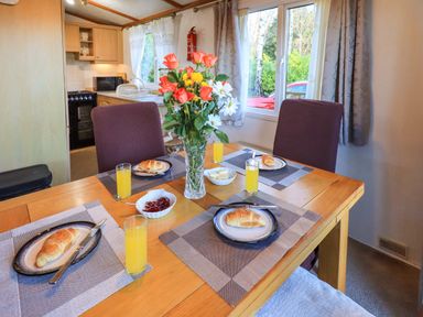 A dining table set with croissants orange juice and flower vase in a kitchen area at Lavender Lodge in South Lakeland Leisure Village