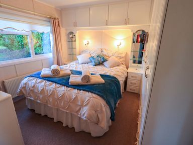 A bedroom with a double bed with folded towels on a blue throw and built in cabinets at Lavender Lodge in South Lakeland Leisure Village