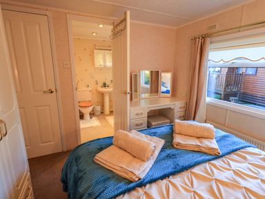 A bedroom with a bed covered with folded towels a dressing table with mirrors and a doorway leading to a bathroom at Lavender Lodge in South Lakeland Leisure Village