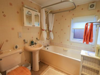 A bathroom with a toilet wooden seat a sink bathtub shower with curtain and a small cabinet with orange towels at Lavender Lodge in South Lakeland Leisure Village