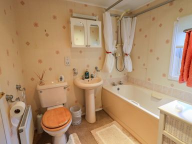 A bathroom with a toilet a pedestal sink and a bathtub with shower curtains at Lavender Lodge in South Lakeland Leisure Village