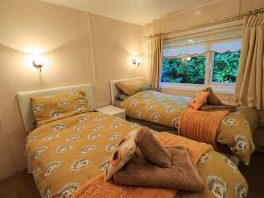 A bedroom with two single beds and a window showing greenery outside at Lavender Lodge in South Lakeland Leisure Village