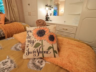 A bedroom with a bed featuring a sunflower pillow and bear patterned bedding at Lavender Lodge South Lakeland Leisure Village