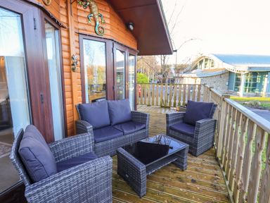 An outdoor wooden deck with a wicker sofa set and glass coffee table at Lavender Lodge South Lakeland Leisure Village
