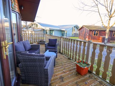 A wooden deck with outdoor furniture and a planter with a building in the background at Lavender Lodge in South Lakeland Leisure Village