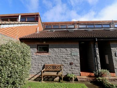 A wooden bench outside a stone house with a tiled roof and a small front garden at Waters Edge in Embleton