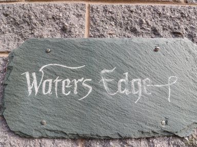 A stone plaque with the words Waters Edge mounted on a stone wall at Waters Edge in Embleton