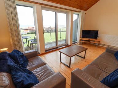 A living room with two leather sofas a wooden coffee table a TV on a stand and sliding glass doors leading to a balcony at Waters Edge in Embleton