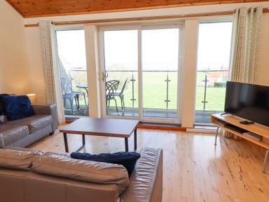 A living room with two sofas a coffee table a television and glass doors leading to a balcony at Waters Edge in Embleton
