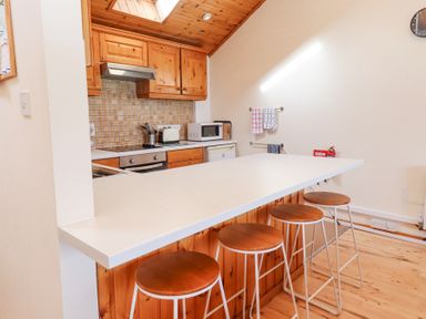 A kitchen with wooden cabinets a countertop with four stools a microwave and a toaster at Waters Edge in Embleton