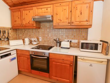 A kitchen with wooden cabinets a built-in oven a dishwasher a kettle a toaster a microwave and kitchen utensils at Waters Edge in Embleton