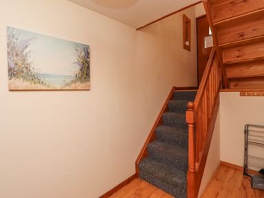 A staircase with carpeted steps and wooden railing in a hallway with a floral painting on the wall at Waters Edge Embleton