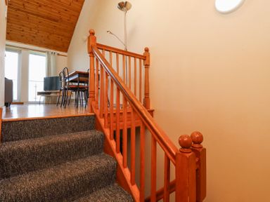 A carpeted staircase leading to a dining area with a table and chairs in a room with wooden ceiling at Waters Edge in Embleton