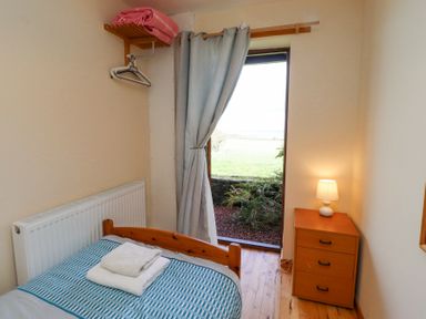 A small bedroom with a single bed folded towels a wooden chest of drawers with a lamp a curtain and a window showing outdoor greenery at Waters Edge in Embleton
