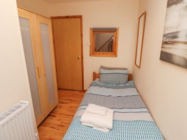 A small bedroom with a single bed with folded towels on it and a wooden wardrobe at Waters Edge in Embleton