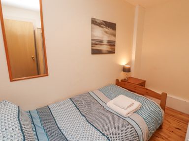 A bedroom with a single bed covered with patterned bedding a bedside table with a lamp a wall mirror and a photograph above the bed at Waters Edge in Embleton