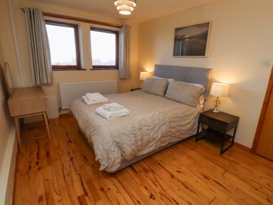 A bedroom with a double bed two bedside tables with lamps a wooden floor and two windows at Waters Edge in Embleton