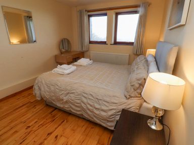 A bedroom with a double bed with folded towels on it two windows with curtains a dressing table and two bedside lamps at Waters Edge in Embleton
