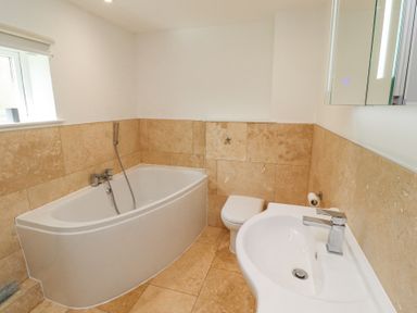 A bathroom with a bathtub toilet and sink with tiled walls and floor at Waters Edge in Embleton
