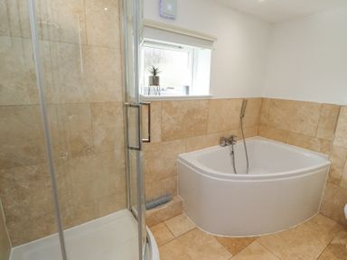 A bathroom with a corner bathtub and a glass shower enclosure with beige tiled walls and floor at Waters Edge in Embleton