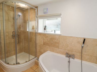 A bathroom with a glass shower enclosure and a bathtub with beige tiled walls at Waters Edge Embleton