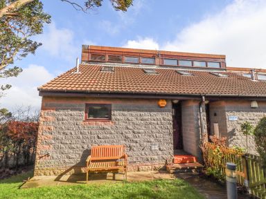 Exterior of a brick house with a tiled roof and a wooden bench outside at Dunstanburgh View in Embleton