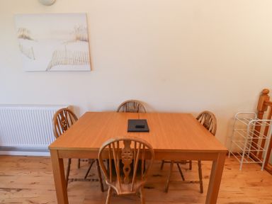 A wooden dining table with four wooden chairs and a remote on top in a room at Dunstanburgh View in Embleton