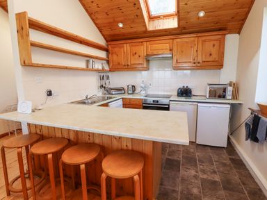 A kitchen with wooden cabinets stools and countertop at Dunstanburgh View in Embleton