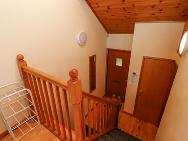 A wooden staircase leading down to a hallway with wooden doors and a wall-mounted mirror at Dunstanburgh View in Embleton