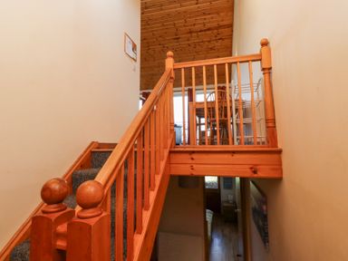 A wooden staircase with carpeted steps leading to a landing with a wooden railing and a dining table with chairs at Dunstanburgh View in Embleton