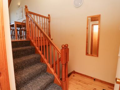 A staircase with carpeted steps and wooden railing next to a wall with a wooden framed mirror at Dunstanburgh View in Embleton