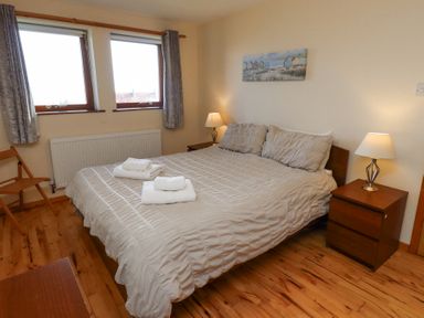 A bedroom with a double bed two bedside tables with lamps folded towels on the bed and two windows at Dunstanburgh View in Embleton