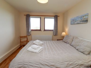 A bedroom with a large bed with towels on it a chair bedside table and two windows at Dunstanburgh View in Embleton