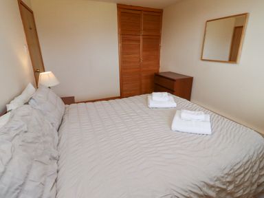 A bedroom with a bed covered with white linens and two sets of folded towels on a bed beside a wooden chest of drawers and wardrobe at Dunstanburgh View in Embleton