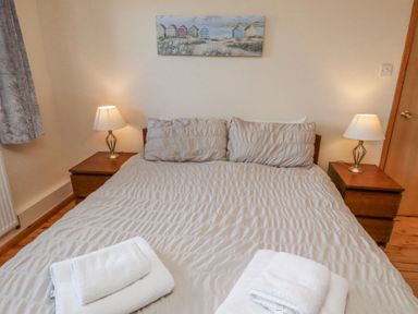 A bedroom with a double bed two bedside tables with lamps and folded towels on the bed at Dunstanburgh View in Embleton