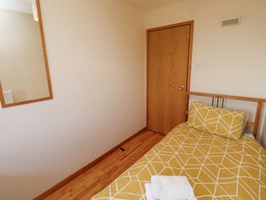 A bedroom with a single bed with yellow patterned bedding a wooden door and a wall mirror at Dunstanburgh View in Embleton