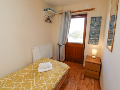 A small bedroom with a single bed with yellow patterned duvet a wooden door a side table with a lamp a wall mirror and a wall decoration at Dunstanburgh View in Embleton