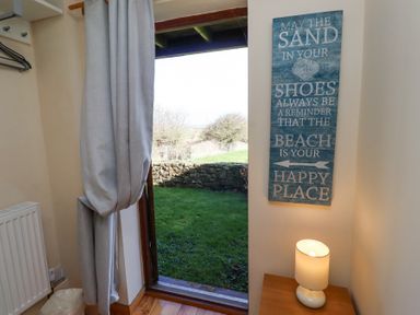 A doorway with a curtain and outdoor view with a wall sign and a lamp on a wooden table in a room at Dunstanburgh View Embleton