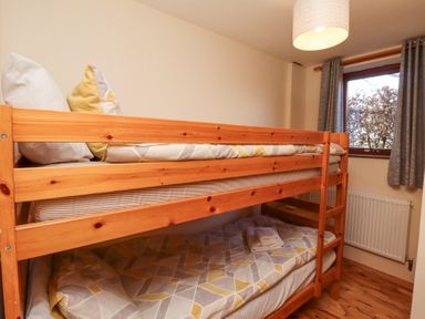 A small bedroom with wooden bunk beds and a window with curtains at Dunstanburgh View in Embleton