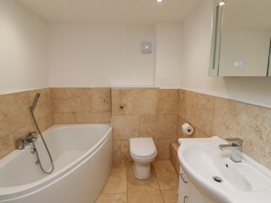 A bathroom with a corner bathtub a toilet a sink with a faucet and a wall mirror cabinet at Dunstanburgh View in Embleton