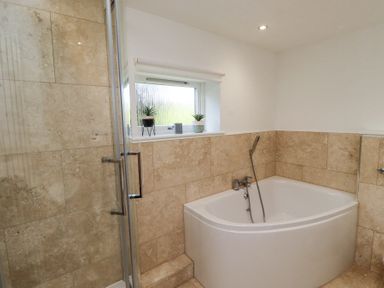 A bathroom with a corner bathtub a glass shower enclosure and two small plants on the windowsill at Dunstanburgh View in Embleton