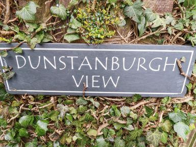 A sign with the text Dunstanburgh View surrounded by green ivy leaves and branches at Dunstanburgh View in Embleton