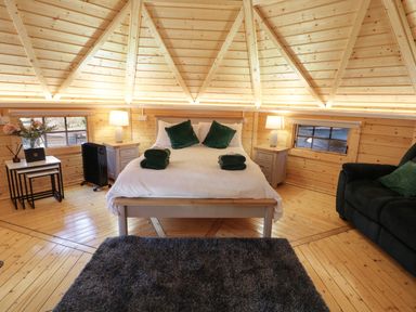 A bedroom with a bed a gray rug a black sofa and wooden walls at The Hideaway in Dungiven Londonderry