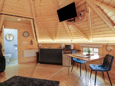 A kitchen and dining area with a wooden table and two chairs a wall-mounted television and a door leading to a bathroom at The Hideaway in Dungiven Londonderry
